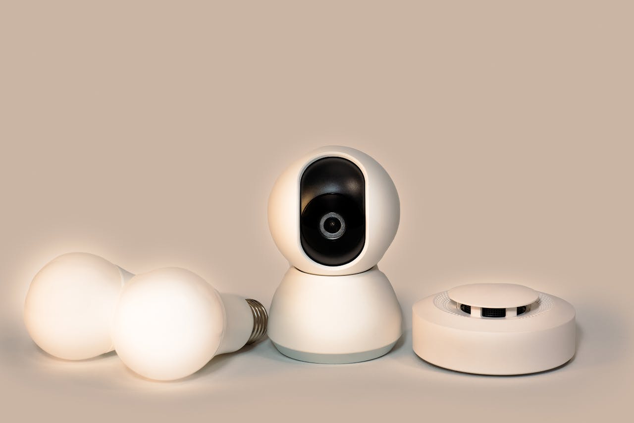 A collection of modern smart home gadgets including a CCTV camera, LED bulbs, and a smoke detector.